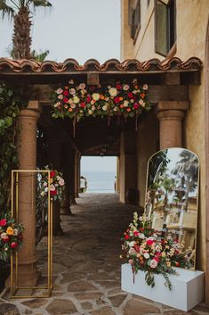 an archway decorated with flowers and greenery next to a building on the beach side