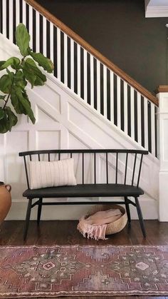 a wooden bench sitting under a stair case next to a potted plant on top of a rug