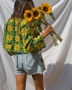 a woman holding sunflowers in front of a white backdrop and wearing a green jacket