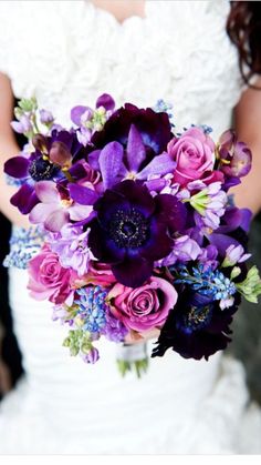 a bride holding a bouquet of purple flowers in front of her wedding cake and wine glasses