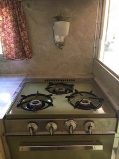 a green stove top oven sitting inside of a kitchen next to a window with curtains