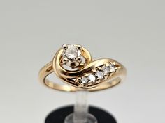 a gold ring with two diamonds on top and a black stand in the foreground