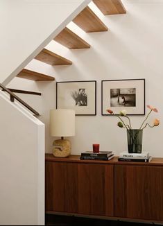 there is a vase with flowers on the table next to stairs and pictures above it