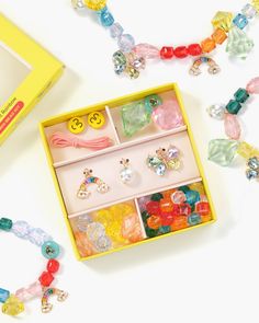 a yellow box filled with lots of colorful beads and bracelets on top of a white table