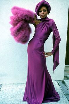 a woman in a long purple dress holding a large pink feather and posing for the camera