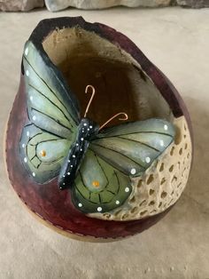 a ceramic butterfly sitting on top of a piece of wood with holes in it's wings