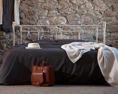 a bed sitting next to a stone wall with clothes hanging on the rails and a purse