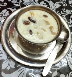 a silver bowl filled with food on top of a metal plate next to a spoon