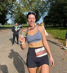 a woman is smiling and holding up her medal as she walks down the street with other people in the background