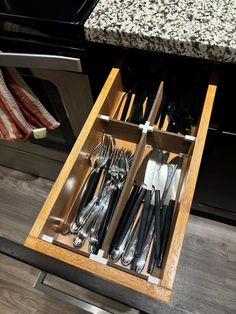 an open drawer with utensils and silverware in it next to a stove