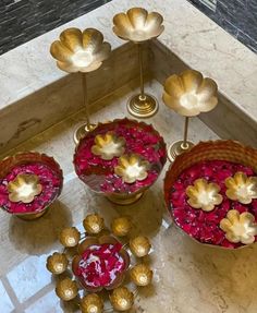 four vases filled with flowers on top of a marble counter next to gold candles