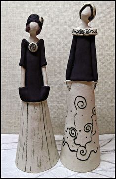 two ceramic figurines sitting next to each other on a white cloth covered surface