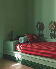 a bed with red sheets and pillows in a green room next to two mirrors on the wall