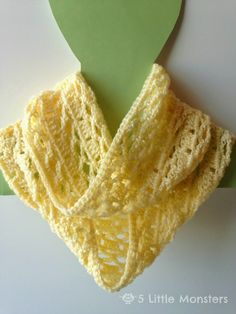 a crocheted yellow scarf hanging from a green hook on a white table top