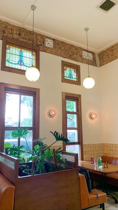 the interior of a restaurant with tables and couches, potted plants in front of two windows