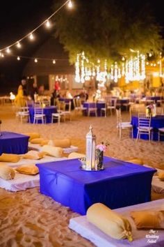 tables and chairs set up on the beach for an outdoor wedding reception with lights strung overhead