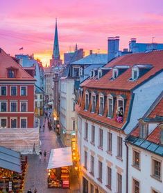 an aerial view of a city street with buildings and people walking on the sidewalk at sunset