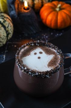 a cup filled with hot chocolate sitting on top of a table next to pumpkins