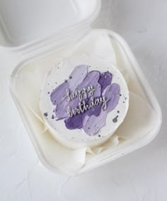 a birthday cake with purple icing in a white container