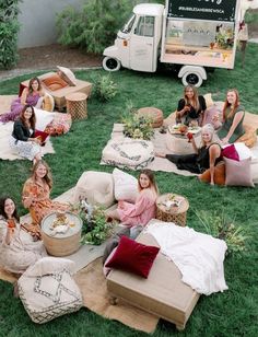 a group of women sitting on top of a lush green field next to a truck