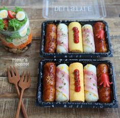 two plastic trays filled with food next to a fork and utensil on a wooden table