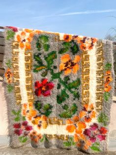 an old rug with flowers on it is hanging from a wooden bench in front of a building