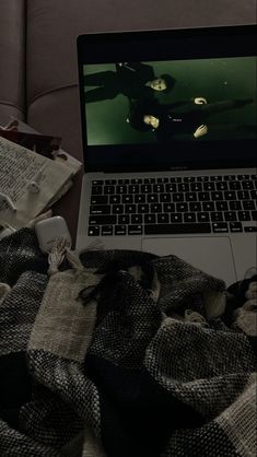 an open laptop computer sitting on top of a bed next to a pile of books