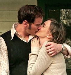 a man and woman kissing each other in front of a house with green door behind them