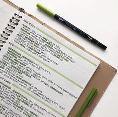 a notebook with some writing on it next to a green pen and a black ballpoint pen