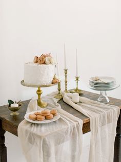 a table topped with a white cake and two plates filled with cookies on top of it