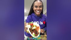 a woman is smiling while holding a taco in front of her face and wearing a purple hoodie