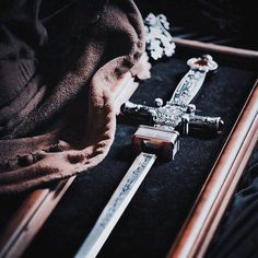 two swords laying on top of a table next to a cloth and other items in a wooden frame