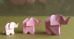 three pink origami elephants standing next to each other on a green surface with flowers in the background