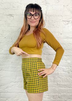 a woman wearing glasses standing in front of a white brick wall with her hands on her hips