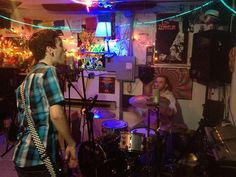 two young men are playing drums in a room with lights and posters on the wall