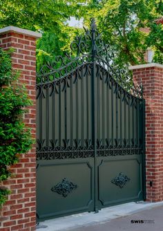 an iron gate in front of a brick wall and green plants on the side of it