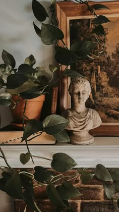 there is a busturine sitting on the mantle next to some books and a potted plant