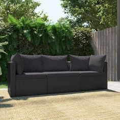 a black couch sitting on top of a rug next to a wooden fence and trees