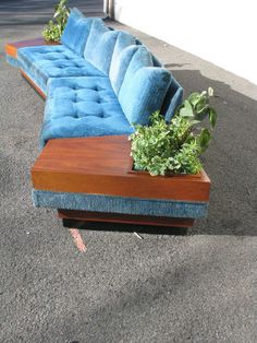 a blue couch sitting in the middle of a parking lot with plants growing on it