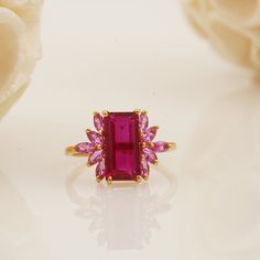 a close up of a ring with a pink stone on it and flowers in the background