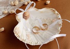 two gold wedding rings sitting on top of a seashell with white ribbon and pearls