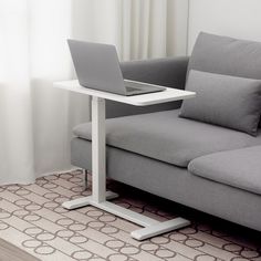 a laptop computer sitting on top of a white table next to a gray couch in a living room