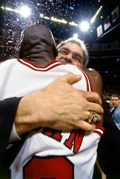 two men hugging each other in the middle of a basketball court with lights behind them