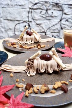 two plates with desserts on them sitting on a table next to leaves and cups