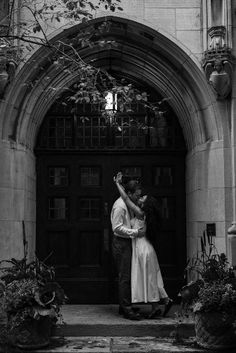 black and white photograph of a couple embracing in front of an old church door with ivy growing around it