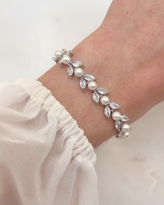 a woman's hand wearing a bracelet with white pearls and crystal leaves on it