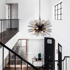 an elegant chandelier hangs from the ceiling in this white foyer with wood flooring