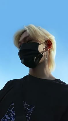 a blonde woman wearing a black face mask against a blue sky with her hair pulled back