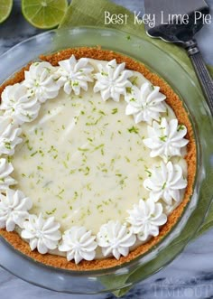 a pie with white frosting and limes on the side sitting on a glass plate