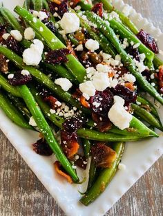 a white plate topped with green beans covered in feta cheese and cranberries